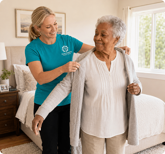 Caregiver helping an older woman put on a cardigan